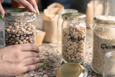 Geri dönüşümlü cam kavanozlar kullanarak nohut, fıstık, fasulye vs. gibi yiyecekleri toplayan bir kadın. Azaltma, yeniden kullanma, geri dönüşüm kavramı.