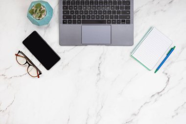 Dizüstü bilgisayarı, akıllı telefonu, not defteri, gözlüğü ve sulu bitkisi olan küçük işletmelerin en küçük masa üstü görüntüsü. Serbest ve ev ofis kavramı. Boşluğu aşağıya kopyala