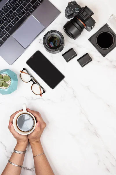 stock image Photographer white marble desk with copy space on right holding coffee with hands. Vertical top view shot