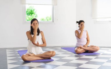 Two Latin yogi woman doing Nadi Shoddana Pranayama with Alternate Nostril breathing. Minimalist bright background. Selective focus