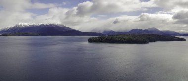Karla kaplı tepeleri olan bir dağla çevrili bir adanın panoramik manzarası