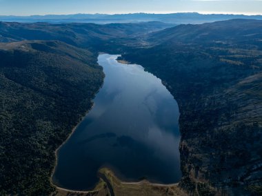 Rucachoroi Gölü 'nün havadan görünüşü açık gökyüzünün altında ağaçlarla çevrili orman tepeleri ve uzak dağ sıraları. Neuquen, Arjantin