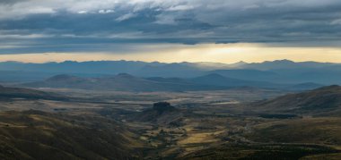 Dağlık arazi, dramatik bulutlu bir gökyüzü altında, engebeli arazisi engebeli vadileri ve uzak sıradağları olan kara bulutlar. Neuquen, Arjantin