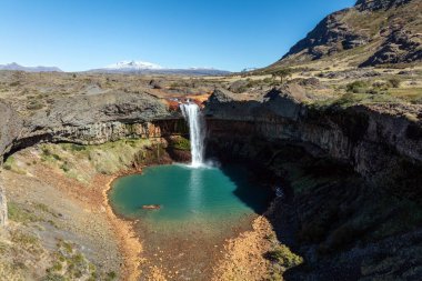 Salto del Agrio şelalesi, karla kaplı Copahue volkanı ile çevrili bir turkuaz havuza dalıyor. Neuquen, Arjantin