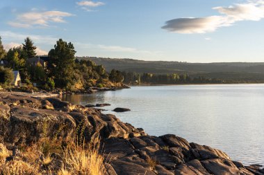 Villa Peheunia, Neuquen, Patagonya, Arjantin 'de bulutlu bir gökyüzünün altında ormanlık tepeleri olan sakin bir göl kıyısında.