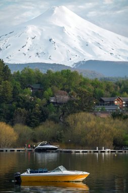 Gölün üstünde karla kaplı bir volkan. Sakin sularda yüzen küçük sarı bir tekne.