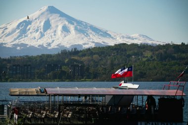 Villarrica karlı zirvesi, göl kenarındaki yanardağ. Şili bayrağı güzel bir sabah manzarası dalgalandırıyor.
