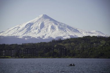 Villarrica volkanı ve gölde balık tutan insanların destansı manzaralı binalar. Araucania, Şili