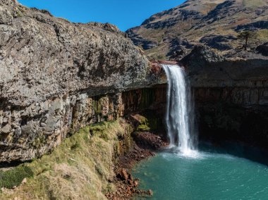 Güçlü Salto del Agrio şelalesi, berrak mavi gökyüzü altında engebeli, dokulu uçurumlar tarafından çerçevelenmiş canlı bir turkuaz havuza dönüşür. Neuquen, Arjantin