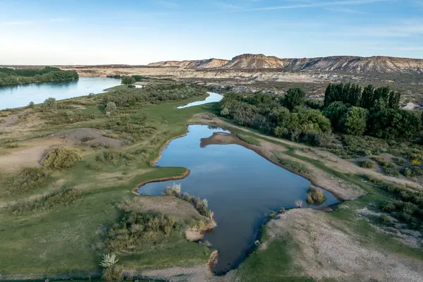 Nehir ve lagünün olduğu yeşil vadi manzarası ve arka planda kumtaşı uçurumlarının destansı manzarası. Paso Cordoba, Rio Negro, Arjantin