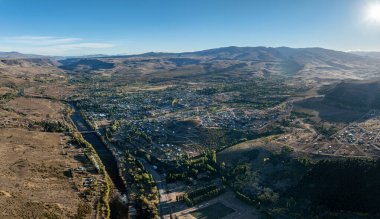 Yüksek açılı çekim: Alumine 'de geniş bir Patagonya vadisinde nehir ve açık bir gökyüzünün altındaki dağları çevreleyen bir kasaba. Neuquen, Arjantin