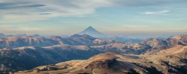 Patagonya 'da bulutlu gökyüzünün altında engebeli, dağlık bir arazide yükselen Lanin volkan dağının panoramik manzarası. Uzakta Los Andes dağları var