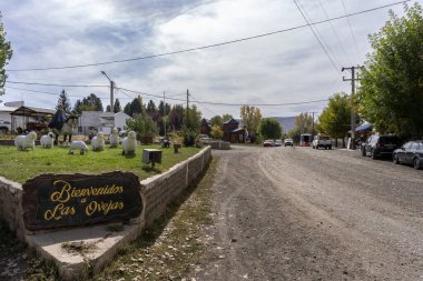 Las Ovejas 'ın karşılama işareti, bulutlu bir gökyüzünün altında toprak yolu ve binaları olan kırsal bir kasabanın girişini gösteriyor. 9 Nisan 2025. Las Ovejas, Neuquen, Arjantin