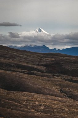Lanin volkanının uzak karla kaplı zirvesi bulutlu bir gökyüzünün altında uçsuz bucaksız, dalgalı Patagonya manzarasının üzerinde yükselir. Neuquen, Arjantin