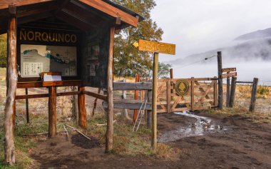 Tahta tabela, Patagonya 'daki sisli bir göle doğru giden bir patikayla Norquinco girişini işaret ediyor. 13 Nisan 2025. Lanin Ulusal Parkı, Neuquen, Arjantin