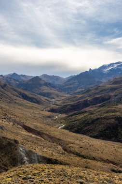 Sarmal nehir Patagonya 'da bir vadi boyunca akar, bulutlu bir gökyüzünün altında dağlar görülebilir. Alüminyum, Neuquen, Arjantin