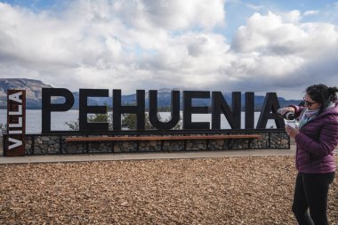 Kadın, arka planda Patagonya 'da bulutlu bir gökyüzünün altında görülebilen bir göl ve dağlarla birlikte, büyük bir 