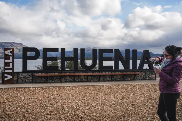 Kadın, arka planda Patagonya 'da bulutlu bir gökyüzünün altında görülebilen bir göl ve dağlarla birlikte, büyük bir 