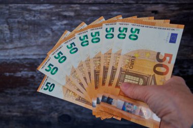 Bir kadın eli, kırsal bir ahşap zemine karşı 50 avroluk banknotların hayranını gösteriyor.