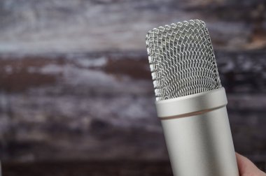 Kırsal bir ahşap arka planda mikrofonu tutan bir elin yakın çekimi..