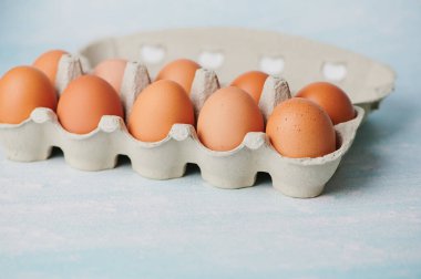 Bir kutuda bir düzine kahverengi yumurta var. Yumuşak mavi bir zemine kurulmuş. Yumuşak kabuklarını sergiliyorlar..