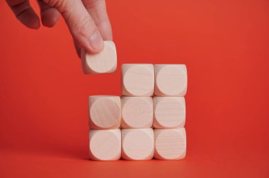 Koyu kırmızı bir yüzey üzerine yığılmış blokların üzerine tahta bir blok yerleştirir..