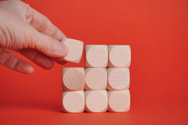 A hand places a wooden block in position on a vivid red background, creating a structure.