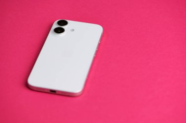 Mainz, Almanya - 09 Haziran 2025: Parlak pembe bir yüzey üzerinde uzanan parlak bir elma iPhone 16 minimalist tasarımını vurguluyor. Çift kamera kurulumu ve pürüzsüz bitiş çağdaş teknoloji eğilimlerini yansıtır.