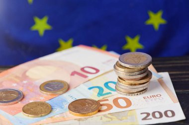 Bir AB bayrağının yanına istiflenmiş avro banknotları ve paraların farklı değerleri, para birimini temsil ediyor.