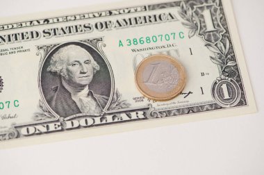 Bir dolarlık banknot, bir avroluk madeni paranın yanında, parasal karşıtlığı gösteren bir yüzey üzerinde yatıyor..