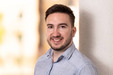 Mavi gömlekli mutlu genç adam dışarıda duruyor ve gülümsüyor.