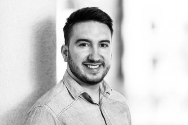 Mavi gömlekli mutlu genç adam dışarıda duruyor ve gülümsüyor.