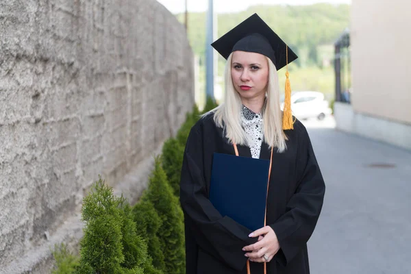 卒業時に自信を持って黒帽とガウンを身に着けている女性ブロンドの大学や高校卒業 — ストック写真