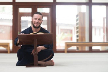 Geleneksel bir Cap Dishdasha takıp, Kuran okuyan Müslüman bir adamın portresi.