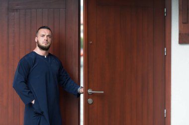 Camide dikilen ve geleneksel bir Cap Dishdasha giyerken kapıyı açan yetişkin bir Müslüman 'ın portresi