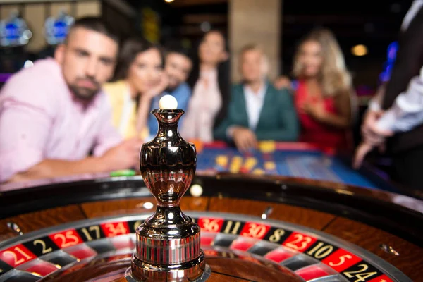 Three Couples Gamble at Night at the Roulette Table in a Casino - Selective Focus on Roulette