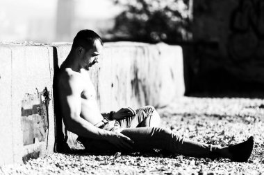 İyi eğitimli vücudunu gösteren genç bir adamın portresi Eski Çatı 'da oturan kaslı atletik vücut geliştirme sporcusu açık hava egzersizlerinden sonra modellik pozisyonu