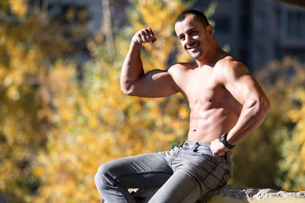 健康的な若い男は 遺跡で強力な曲げ筋肉に座って 筋肉運動体ビルダーフィットネスモデルは 屋外をポーズ — ストック写真