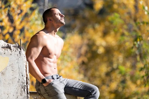 健康的な若い男は 遺跡で強力な曲げ筋肉に座って 筋肉運動体ビルダーフィットネスモデルは 屋外をポーズ — ストック写真