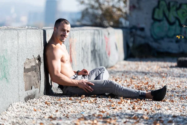 健康な若い男は 古い屋根の上に強力な曲げ筋肉に座って 筋肉運動体ビルダーフィットネスモデルは 屋外をポーズ — ストック写真