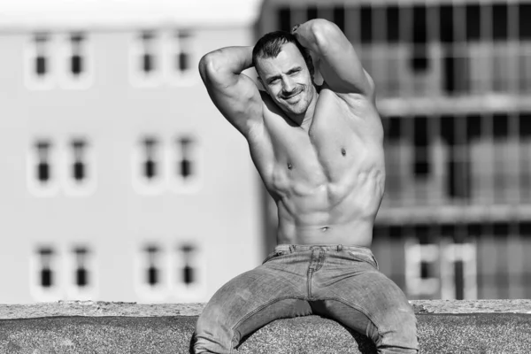 健康な若い男は 古い屋根の上に強力な曲げ筋肉に座って 筋肉運動体ビルダーフィットネスモデルは 屋外をポーズ — ストック写真