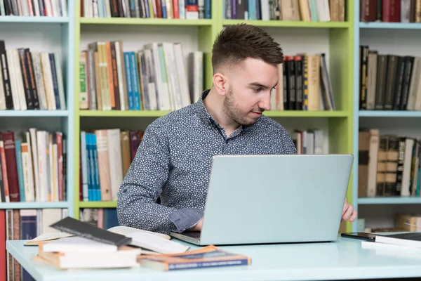 坐在图书馆书桌前的英俊男子 笔记本电脑和桌上的组织者 后面的书籍模糊不清 — 图库照片