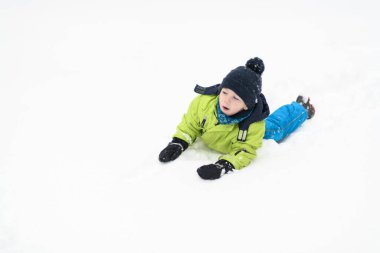 Küçük çocuk kar yağarken dışarıda eğleniyor ve karla oynuyor.