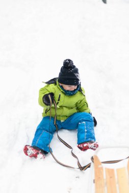 Sıcak elbiseli mutlu çocuk kızakla kayıyor ve düşüyor.
