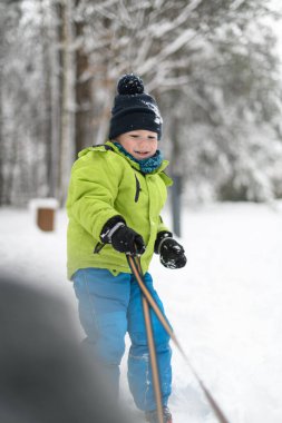 Kar yağışı sırasında dışarıda kızak çeken küçük çocuk.