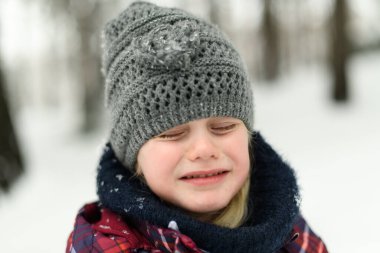 Küçük kız üzgün vakit geçiriyor ve kar yağarken dışarıda karla oynamıyor.