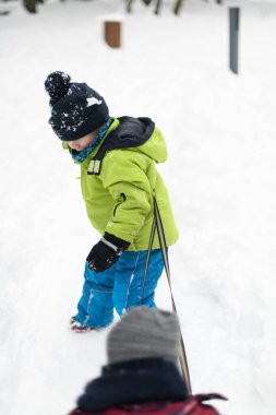 Kar yağışı sırasında dışarıda kızak çeken küçük çocuk.