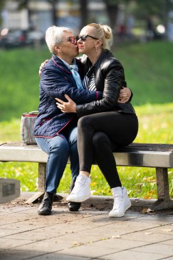 Mavili yaşlı bir kadın ve siyahlı kızı bir sonbahar günü parktaki bankın keyfini çıkarıyorlar. Bu güneşli ve gündelik ortamda aile bağları çok açık.