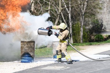 İtfaiyeci koruyucu kask takıyor. Yanan yağ tenekesini söndürmek için köpük püskürtüyor.