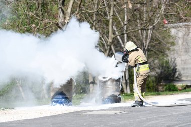Yangını söndürmek için köpük kullanan itfaiyeci dumanlı bir doğal ortamda erimiş yağ tenekesinde.